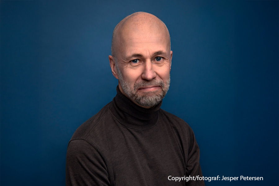 Johan Theorin med en brun polo och turkos bakgrund.
